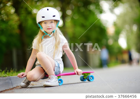 Pretty little girl learning to skateboard on beautiful summer day in a park 37666456