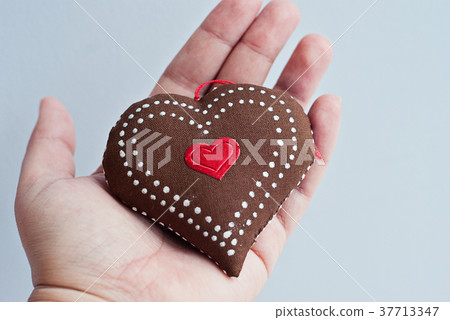 Female hand holds a beautiful soft handmade heart Female hand holds a beautiful soft handmade heart 37713347