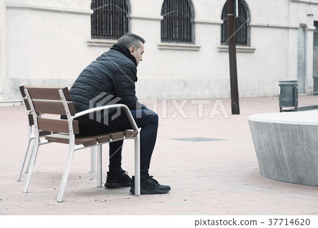 sad man sitting in a bench in the street 37714620