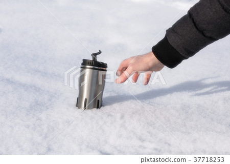 A man's hand reaches for a thermos with hot coffee A man's hand reaches for a thermos with hot coffee 37718253