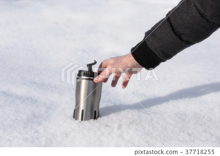 A man's hand reaches for a thermos with hot coffee A man's hand reaches for a thermos with hot coffee 37718255