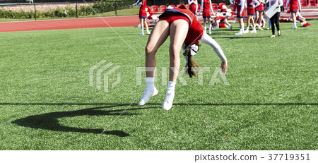 Cheerleader practicing a back flip on green turf Cheerleader practicing a back flip on green turf 37719351