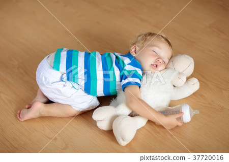 Baby sleeping on floor with toy and milk bottle. 37720016