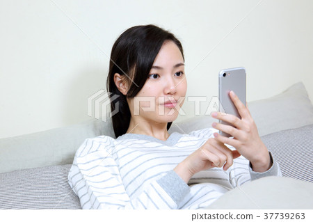 A woman watching a smartphone in her bedroom A woman watching a smartphone in her bedroom 37739263