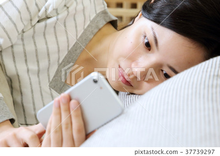 A woman watching a smartphone in her bedroom 37739297