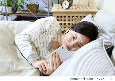 A woman watching a smartphone in her bedroom A woman watching a smartphone in her bedroom 37739299