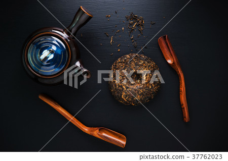 Tea pot and green dry tea on black table 37762023