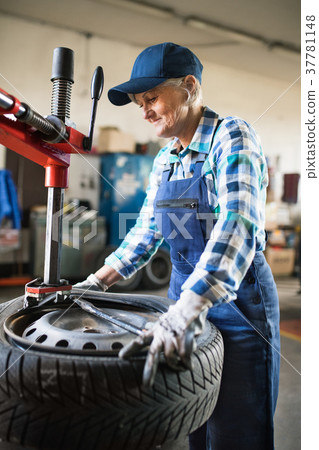 Senior female mechanic repairing a car in a garage Senior female mechanic repairing a car in a garage 37781148