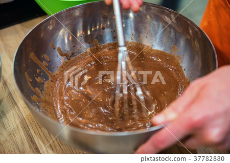 Hands mix chocolate dough with whisk 37782880