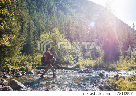 Hiker with backpack crossing mountain river 37818997