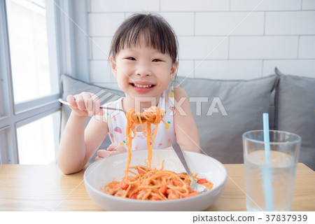 Little girl using fork eating spaghetti by herself 37837939