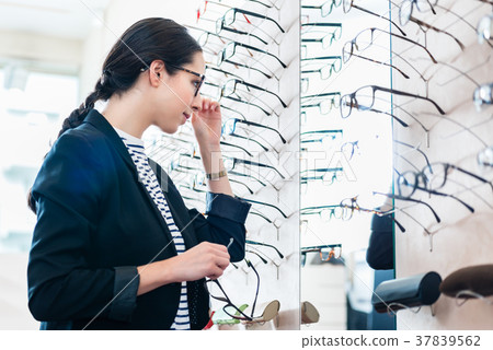 Woman taking glasses off shelf in optician shop 37839562
