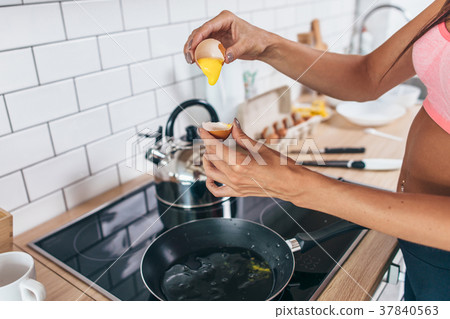 Fit woman in kitchen cracking egg into frying pan. 37840563