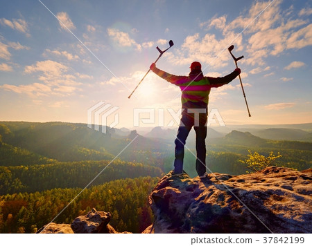 Hiker with medicine crutch above head achieved top Hiker with medicine crutch above head achieved top 37842199