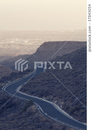 Alone cyclist on winding mountain road. 37843054
