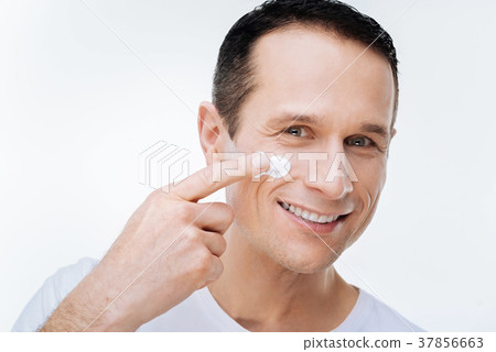 Positive nice man using facial cream 37856663