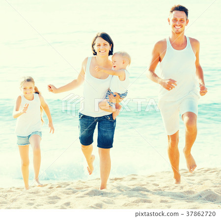 family of four running on sandy beach on sunny weather family of four running on sandy beach on sunny weather 37862720