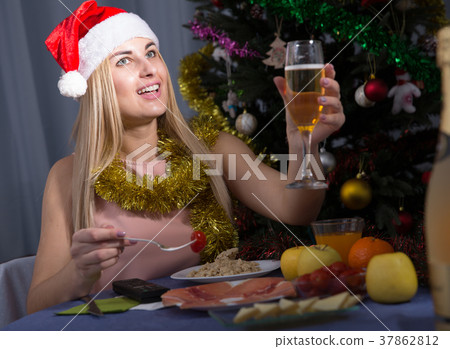 Young female is watching TV and sitting with champagne in New Year night Young female is watching TV and sitting with champagne in New Year night 37862812