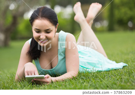 young girl using digital tablet while lying in green spring garden 37863209