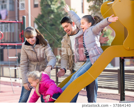Happy family at sliding board outdoors . Happy family at sliding board outdoors . 37864140