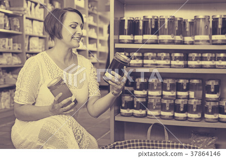 Woman choosing honey from assortment in drugstore Woman choosing honey from assortment in drugstore 37864146