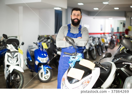 cheerful man worker displaying various motorcycles in workshop cheerful man worker displaying various motorcycles in workshop 37864269