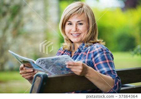 Portrait of mature woman sitting on bench and reading book in garden Portrait of mature woman sitting on bench and reading book in garden 37864364