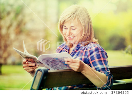 Portrait of mature woman sitting on bench and reading book in garden Portrait of mature woman sitting on bench and reading book in garden 37864365