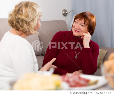 Smiling mature lady with female friend at home Smiling mature lady with female friend at home 37864477