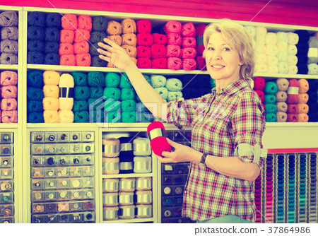 portrait of mature female customer standing next to shelf with knitting yarn in shop portrait of mature female customer standing next to shelf with knitting yarn in shop 37864986