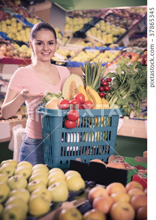 woman with basket with fresh greengrocery enjoying purchases in vegetable store 37865345
