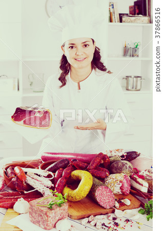 Girl cook costs near table on which sausages and smoked meat Girl cook costs near table on which sausages and smoked meat 37866516