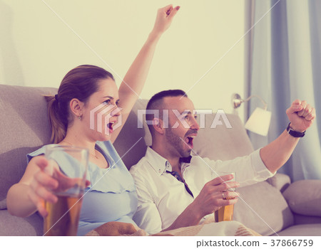 Young female and her husband are faning in time watching football 37866759