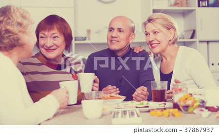 Smiling aged friends are sitting at table with tea and talking about life 37867937