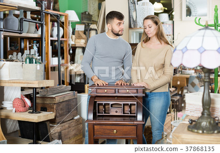Thoughtful couple choosing vintage writing cabinet 37868135