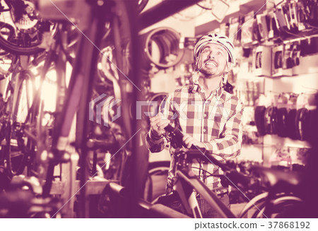admiring man in helmet chooses for himself sports bike in bicycle shop admiring man in helmet chooses for himself sports bike in bicycle shop 37868192
