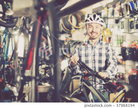 positive man in helmet chooses for himself sports bike in bicycle shop positive man in helmet chooses for himself sports bike in bicycle shop 37868194