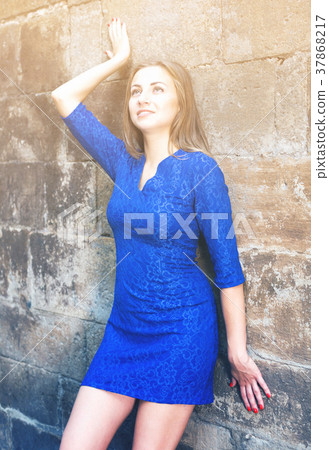Young woman is posing in blue dress near old wall Young woman is posing in blue dress near old wall 37868217