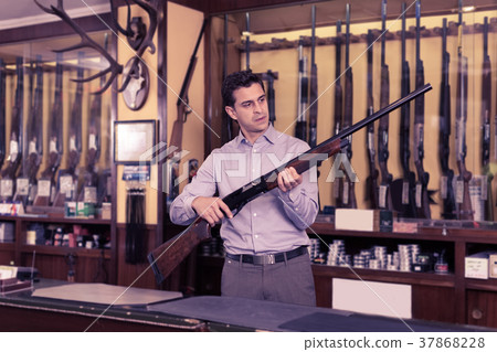 Male standing with shotgun indoors in hunting shop Male standing with shotgun indoors in hunting shop 37868228