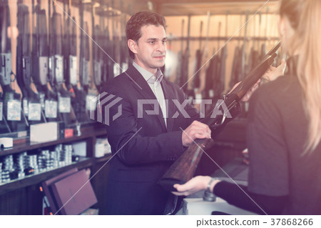 Salesman in gun shop showing rifle to female client Salesman in gun shop showing rifle to female client 37868266