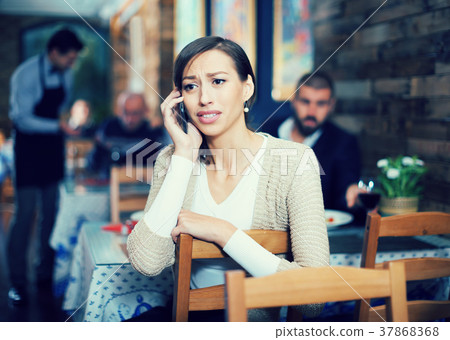 upset female holding mobile in the restaurant 37868368