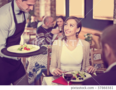 Waiter male bringing food for male and female 37868381