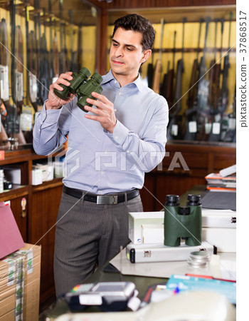 Serious man choosing new binocular for hunting in store with hunt equipment Serious man choosing new binocular for hunting in store with hunt equipment 37868517