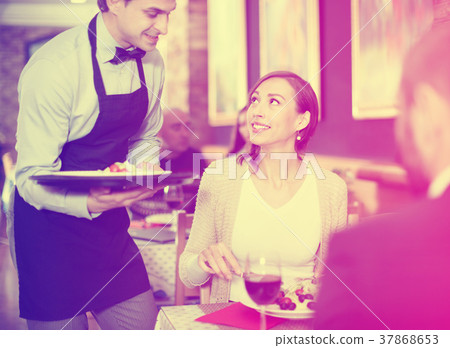 Waiter with dishes serving man and woman friendly company indoors 37868653