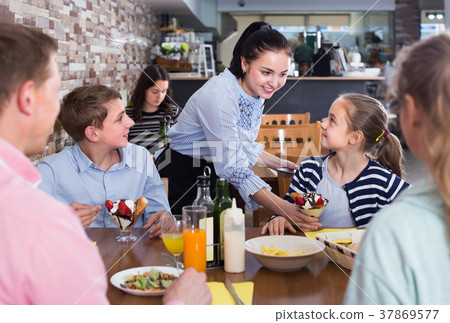 Young brunette waitress serving joyous family in family cafe Young brunette waitress serving joyous family in family cafe 37869577