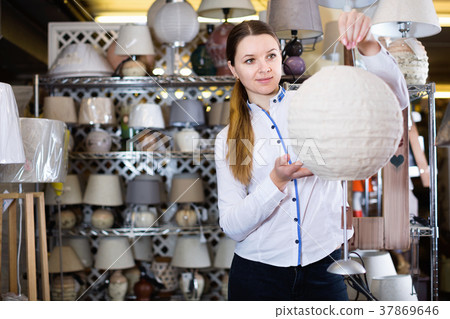 Girl is choosing modern table lamp in furniture store. 37869646