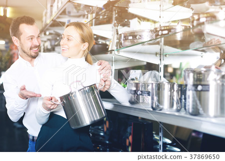 Couple examining various saucepans in dinnerware store 37869650