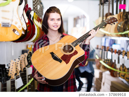 teenage customers deciding on suitable acoustic guitar in guitar shop 37869918