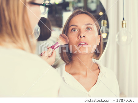 female makeup artist applying cosmetics for woman female makeup artist applying cosmetics for woman 37870163