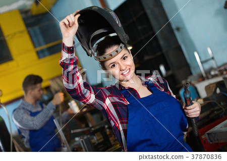 Girl worker is standing in protection helmet in workshop. Girl worker is standing in protection helmet in workshop. 37870836